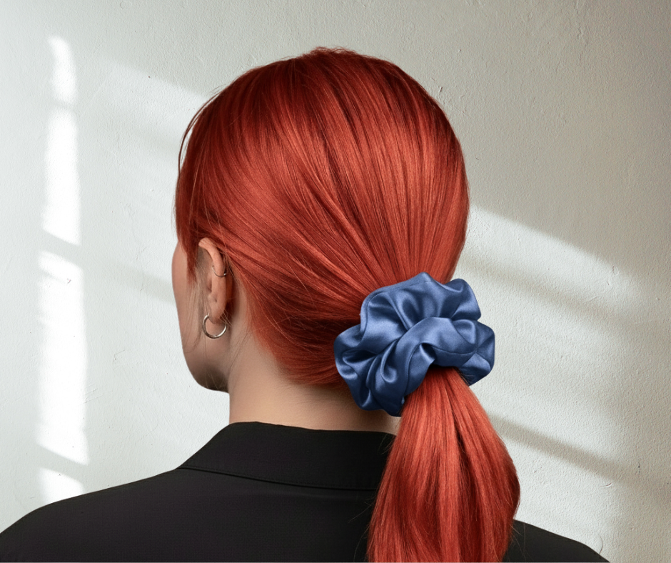 Person with red hair tied in a ponytail with a pacific blue colored silk scrunchie, against a light background.