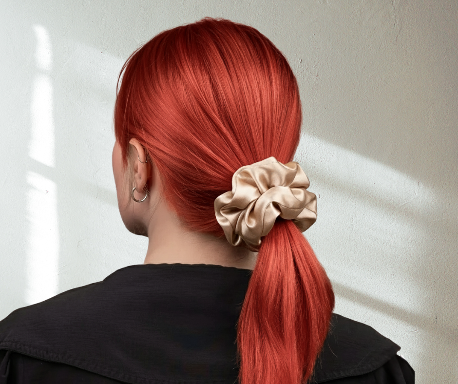 silk scrunchie in champagne color on red-headed model with ponytail against whitish background.