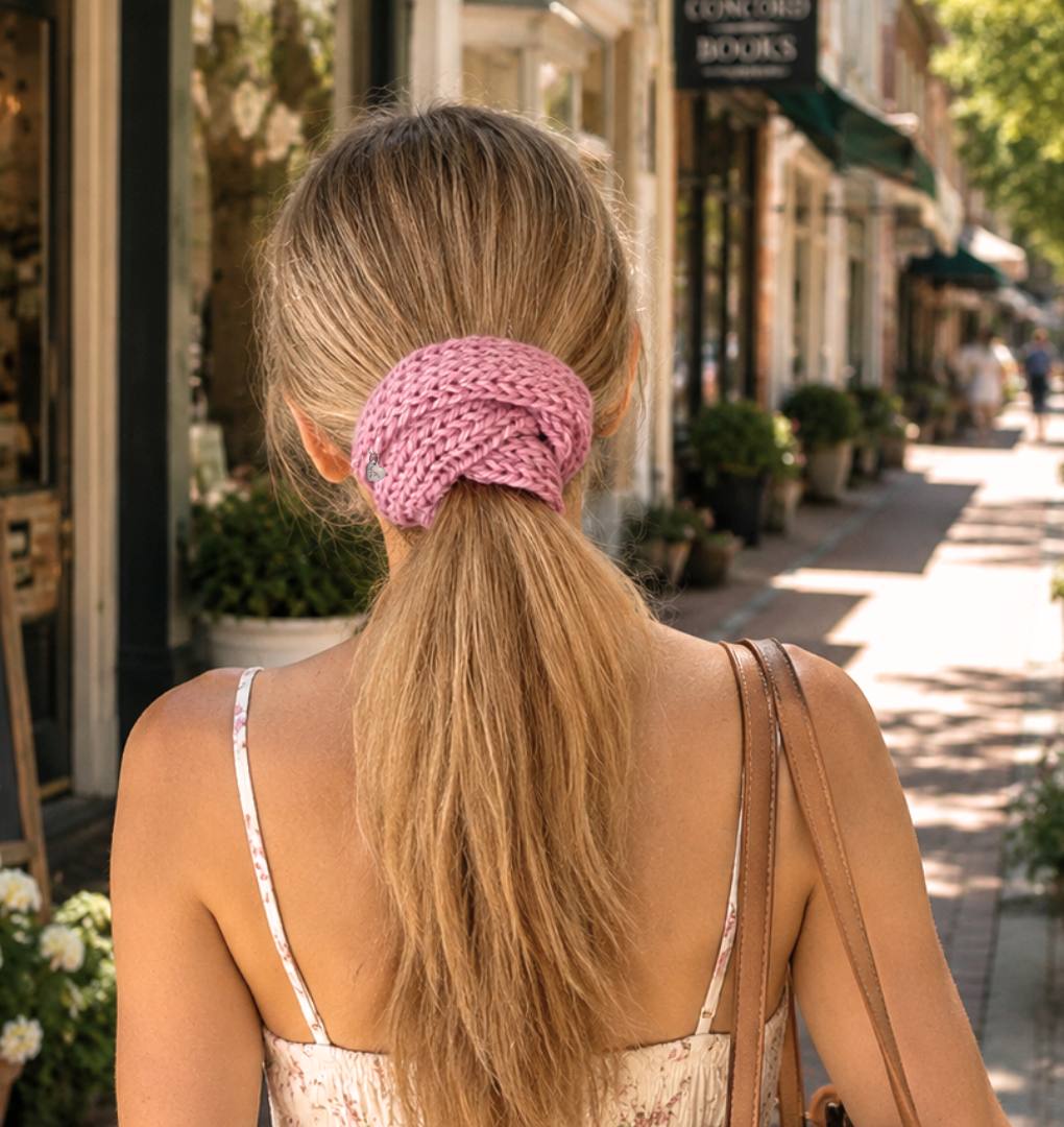 Woman with a pink hair tie in a ponytail walking down a street lined with shops and plants.