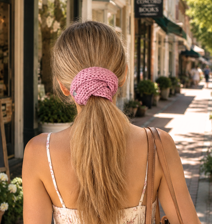 Woman with a pink hair tie in a ponytail walking down a street lined with shops and plants.