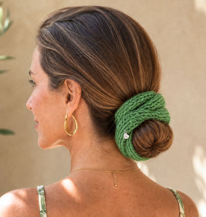 Woman with a green knitted hair accessory in her bun against a beige background