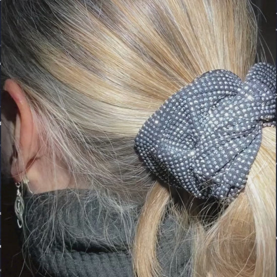 Closeup of model wearing silver-white rhinestone scrunchie, night scene with stars.