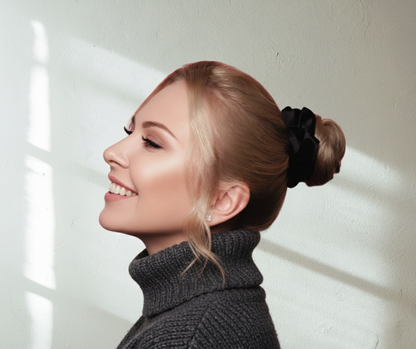 Onyx black colored silk scrunchie on close-up of a model in grey sweater looking up on light background.
