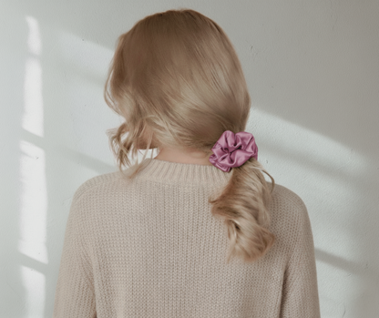 Mauve colored silk scrunchie in the hair of a model with low ponytail on light background.