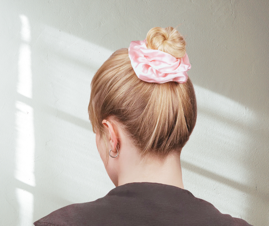ballerina pink silk scrunchie on model with bun and black top against stucco wall