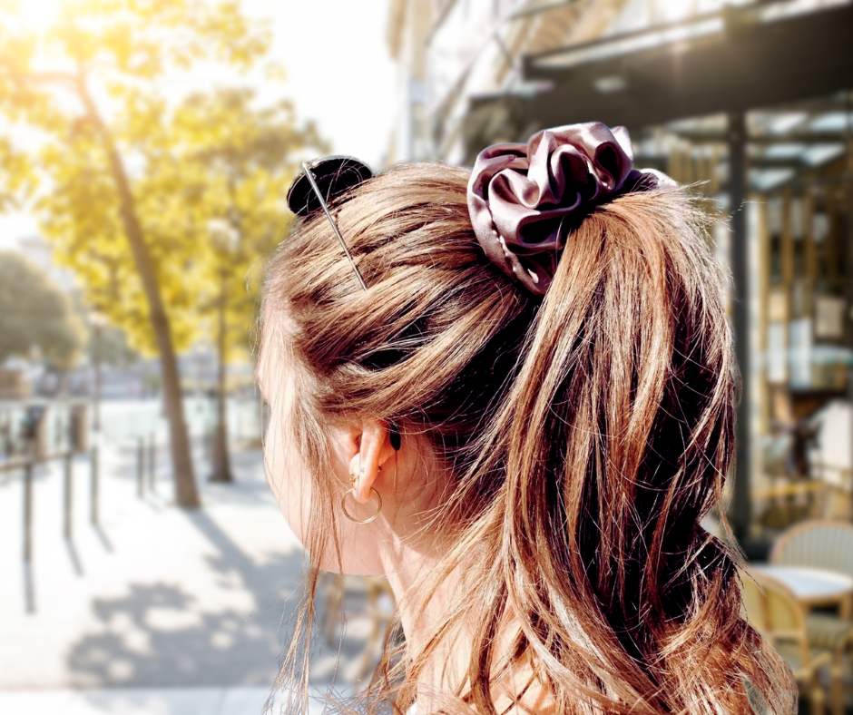 Woman with dark mauve silk scrunchie in her hair standing  outdoors on a sunny day