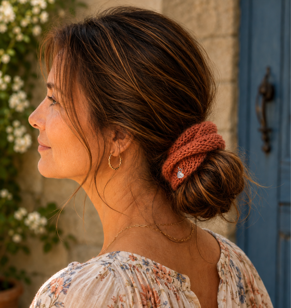 Woman with a knitted terracotta colored scrunchie in her hair, standing outdoors.