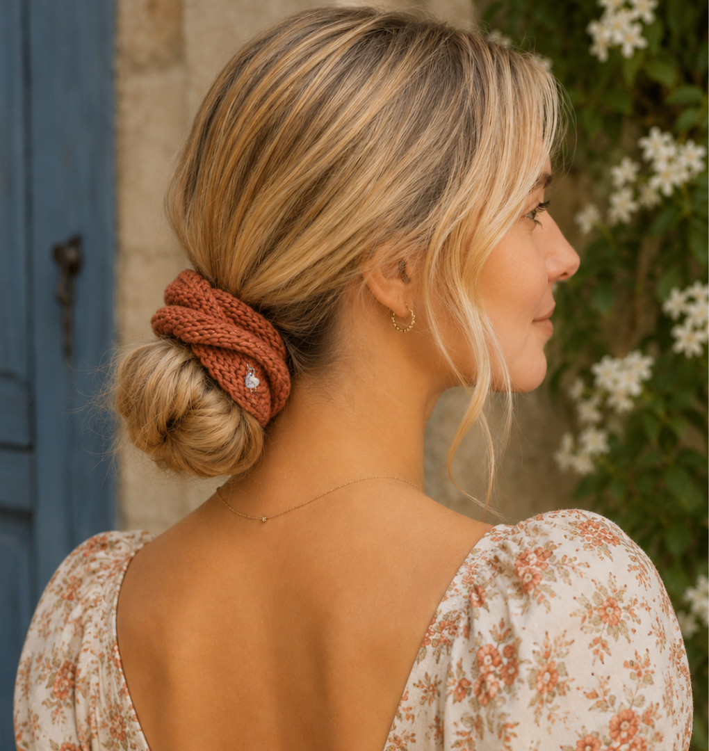 Woman with a styled bun and terracotta scrunchie wearing a floral dress, standing outdoors.
