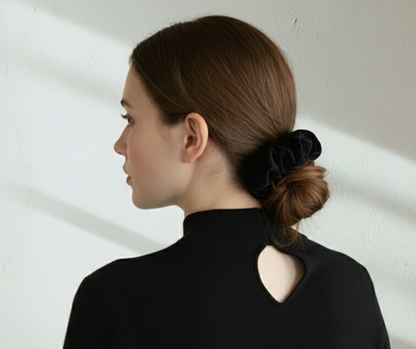 Model with a black silk velvet scrunchie in their hair side viewagainst a light background.