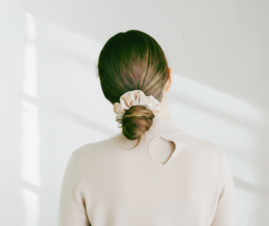 Model with a champagne colored silk velvet scrunchie in their hair against a light colored background. 