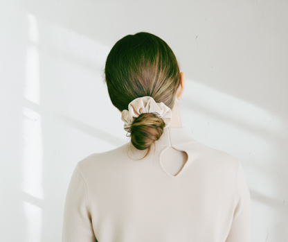 Model with a champagne colored silk velvet scrunchie in their hair against a light colored background. 