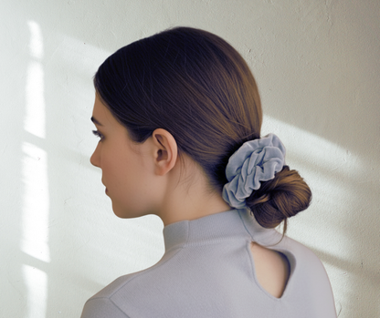 Model with a ice blue silk velvet scrunchie in their hair, side-view,  against a light background. 